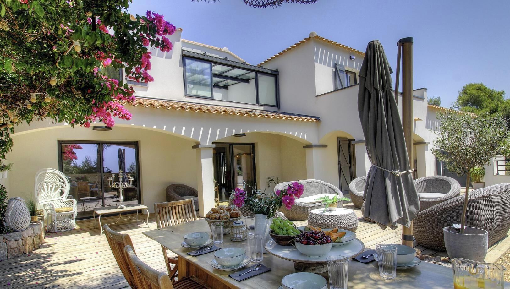 Ein modernes Haus mit Terrasse, Sitzgelegenheit im Freien und einem Esstisch, gedeckt mit Früchten und Blumen.