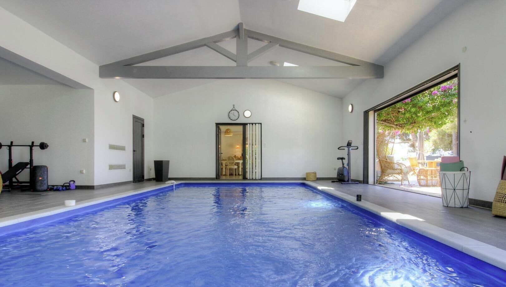 Piscina interior con tragaluz, equipo de ejercicio y vistas al exterior.