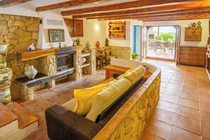 A cozy living room with a stone fireplace, wooden furniture, and a view to an outdoor patio. - Design and stone essence in Costa Brava (Girona)