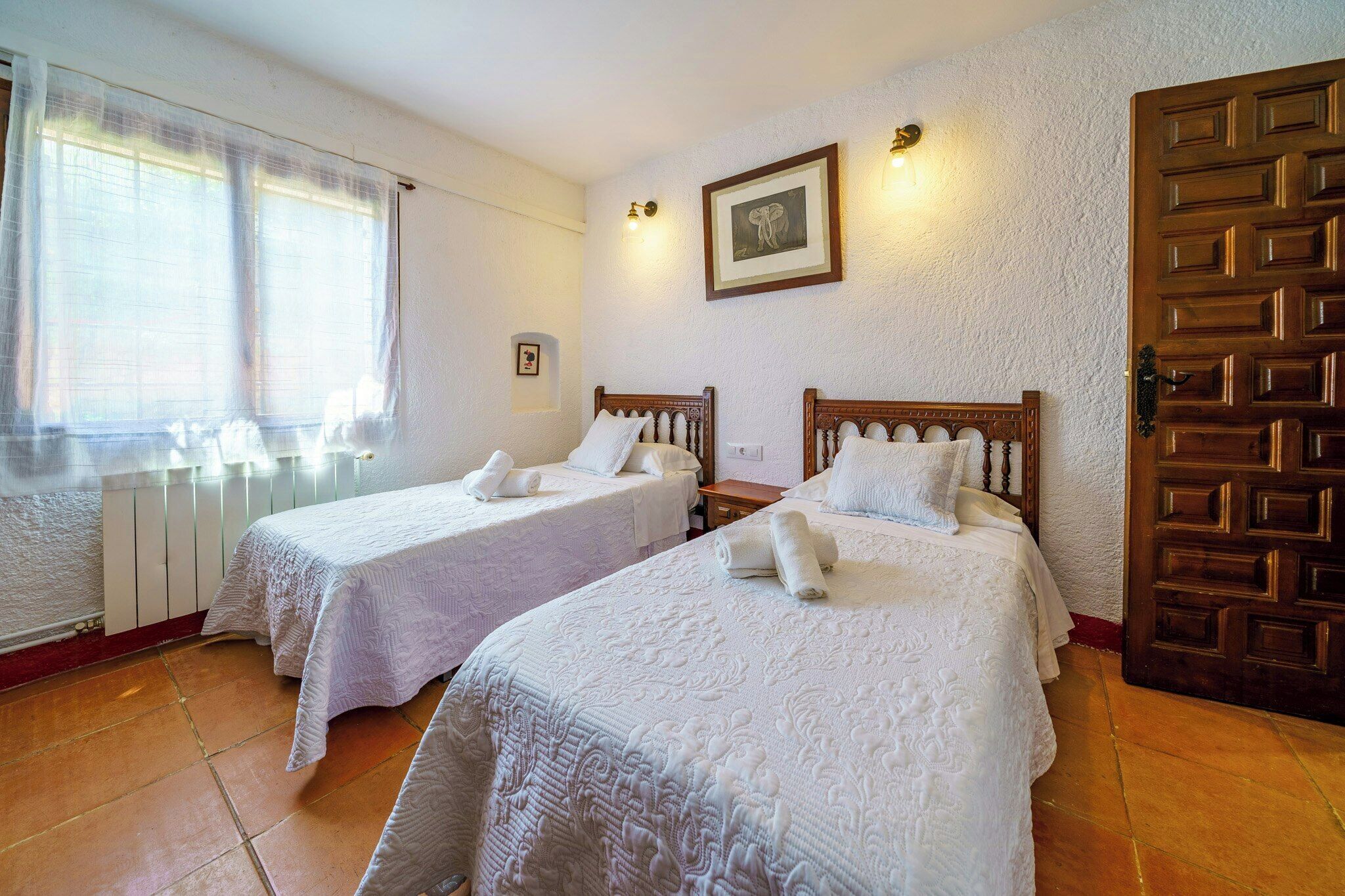 Ein Hotelzimmer mit zwei Betten, einem Heizkörper, einer Holztür und einem gerahmten Bild an der Wand.