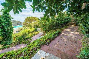 A stone pathway surrounded by lush greenery and a view of a beach. - Design and stone essence in Costa Brava (Girona)