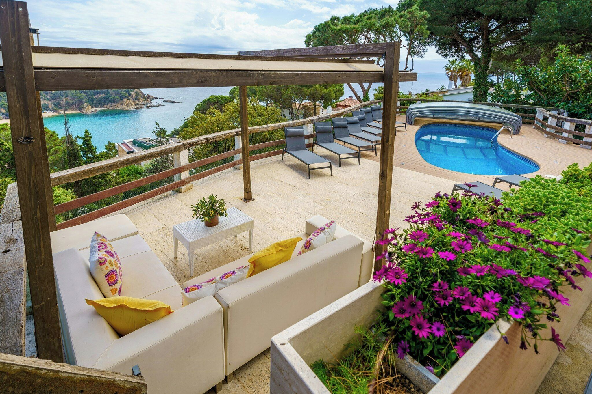 A pool area with lounge chairs, a hot tub, and a view of the sea.