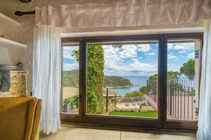 A room with a large window overlooking a coastal landscape, a chair, and a stone wall. - Design and stone essence in Costa Brava (Girona)