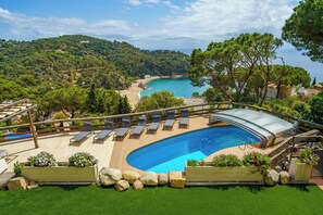 A pool with lounge chairs, a wooden deck, and a view of a beach and forest. - Design and stone essence in Costa Brava (Girona)