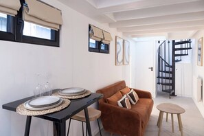 Ein modernes Interieur mit einem für zwei Personen gedeckten Esstisch, einem braunen Sofa und einer Wendeltreppe.