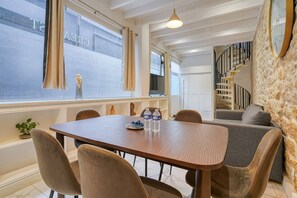 A dining area with a wooden table, chairs, and a view of a building through large windows. - Loft in Sentier - Paris - 6P - 2BR (Paris)