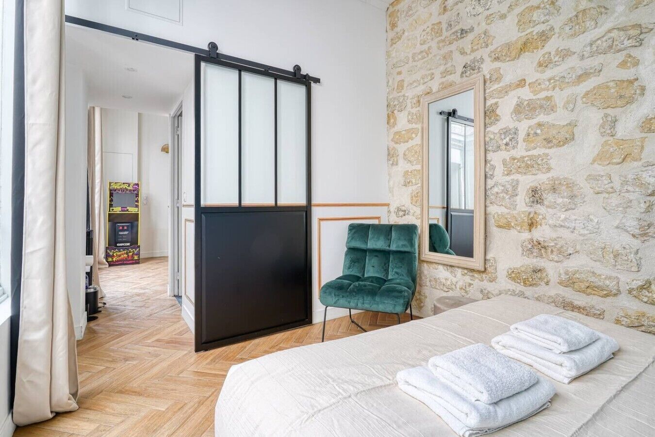 Un dormitorio con una cama, una silla verde, un ventanal corredero y una pared de piedra.