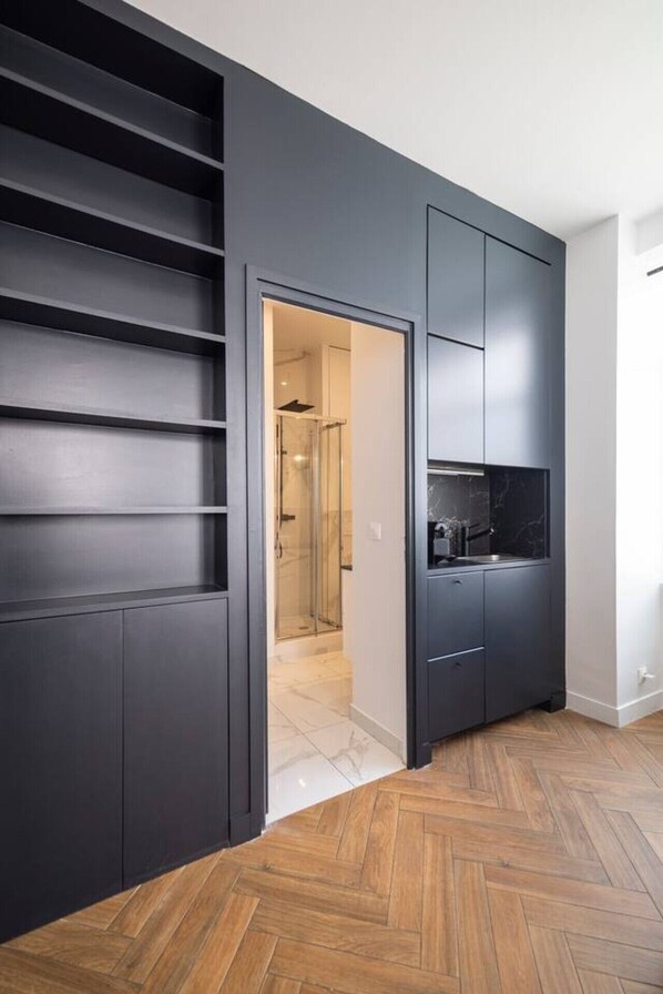 Ein modernes Interieur mit einem Fischgrätparkett, einem dunkelgrauen Kleiderschrank und einer Küchenzeile mit schwarzer Arbeitsplatte.