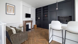 Ein modernes Wohnzimmer mit Kamin, Wandfernseher und Essbereich mit weißen Stühlen.