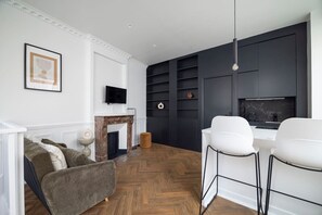 Ein modernes Wohnzimmer mit Kamin, Wandfernseher und Essbereich mit weißen Stühlen.