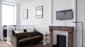 Ein Zimmer mit Kamin, einer Couch, einem darüber montierten Fernseher und gerahmten Bildern an der Wand.