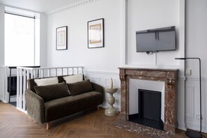 Ein Zimmer mit Kamin, einer Couch, einem darüber montierten Fernseher und gerahmten Bildern an der Wand.