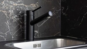 Eine moderne Küche mit einem schwarzen Wasserhahn, einer Edelstahl-Spüle und einer Marmor-Spritzschutzwand.