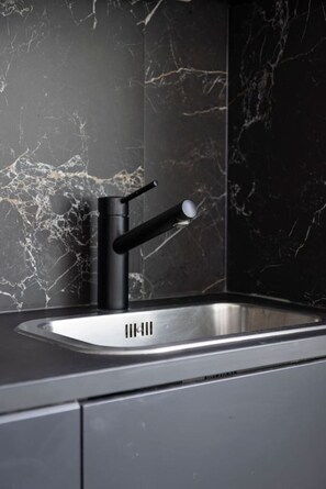 Eine moderne Küche mit einem schwarzen Wasserhahn, einer Edelstahl-Spüle und einer Marmor-Spritzschutzwand.