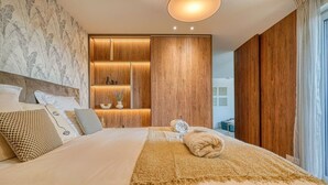 A bedroom with a large bed, wooden paneling, a built-in shelf with decorative items, and a view of the outside. - Bois de Vincennes - Luxury & Balcony - 4P (Saint-Mandé)