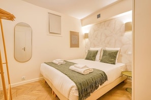 Quarto com cama, espelho, janela e luminária fixada na parede.