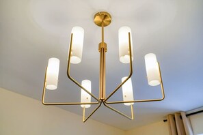 Um candelabro com uma coluna central e braços múltiplos, cada um terminando em uma luminária cilíndrica.