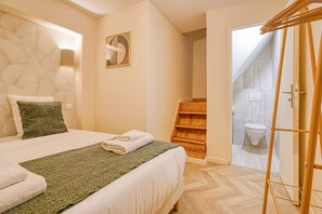Habitación de hotel con cama, un tapete verde, estante de madera, inodoro y zona de ducha.