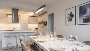 Una cocina moderna con una isla central, taburetes de bar y una zona de comedor preparada para seis personas, con platos y vasos.