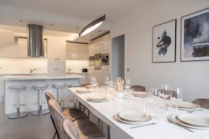 A modern kitchen with a central island, bar stools, and a dining area set for six with plates and glasses. - Spacious 4BR in Paris - 3 Baths - 10 Guests (Montreuil)