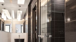 Un baño moderno con cabina de ducha de vidrio, un lavabo negro y piso de color claro.