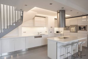 A modern kitchen with a central island, built-in appliances, and a staircase. - Spacious 4BR in Paris - 3 Baths - 10 Guests (Montreuil)