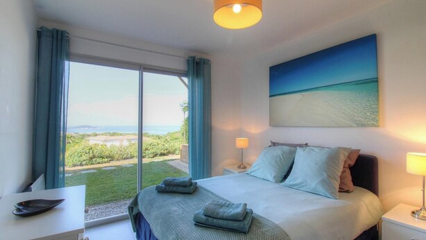 Ein Schlafzimmer mit einem Bett, zwei Nachttischlampen, einem Gemälde und Blick ins Freie.