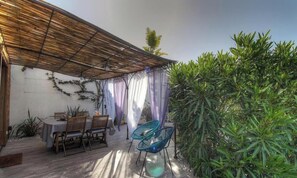 Eine Terrasse im Freien mit einem Holztisch und -stühlen, einer Pergola und üppigem Grün.