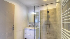 Ein modernes Badezimmer mit Duschkabine aus Glas, einem weißen Waschtisch mit Spiegel und einer gefliesten Duschwand.