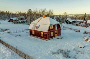 A red wooden house with a snow-covered roof, surrounded by a wooden fence and snow-covered ground. - Red house from 1921 by the Vasaloppet trail (Älvdalen)
