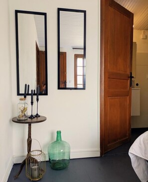 Une pièce avec deux miroirs fixés au mur, une porte en bois, une petite table avec des bougies, un bocal en verre et une bouteille verte.