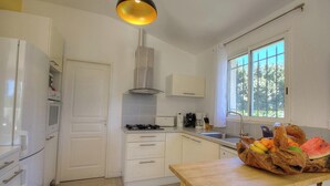 A kitchen with white cabinets, a gas stove, a stainless steel range hood, a window with curtains, and a fruit basket on the counter. - Serenity - SOTTA - Gîte (SOTTA)