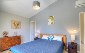 Ein Schlafzimmer mit Bett, Holzschrank, Nachttischen und Wandbildern.