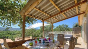 A covered outdoor dining area with a table set for two, chairs, and a view of the surrounding landscape. - Serenity - SOTTA - Gîte (SOTTA)
