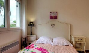 Ein Schlafzimmer mit Bett, Nachttisch, Lampe, Fenster und Wandbild.