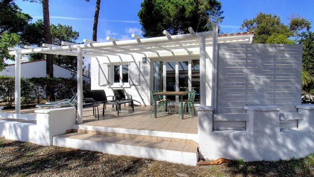 Un patio al aire libre techado con una mesa, sillas, una pérgola y un edificio blanco con ventanas.