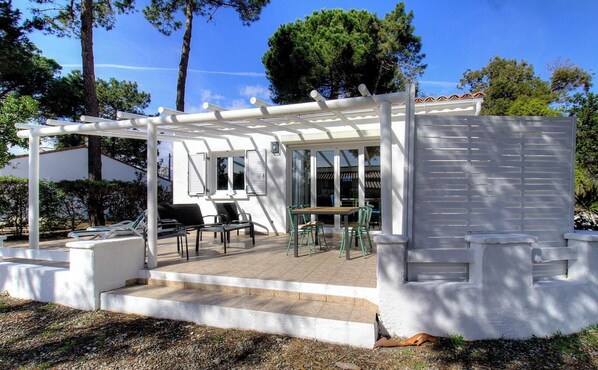 Eine überdachte Terrasse im Freien mit Tisch und Stühlen, einer Pergola und einem weißen Gebäude mit Fenstern.
