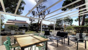 Un patio exterior con una mesa y sillas de madera, una parrilla y una estructura de pérgola.