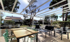 Eine Terrasse im Freien mit Holztisch und -stühlen, einem Grill und einer Pergola.