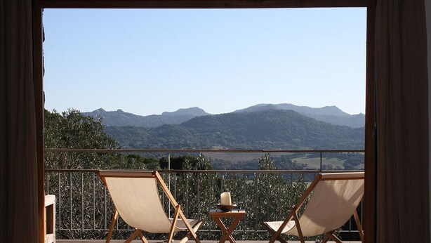 Ein Balkon mit zwei Holzliegen und einem kleinen Tisch, mit Blick auf eine gebirgige Landschaft.