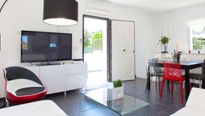 Un salon moderne avec une table basse en verre, un téléviseur, un fauteuil rouge et un coin repas avec un autre fauteuil rouge.