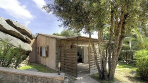 Un bâtiment rustique à la structure en bois, doté d’un mur en pierre et d’un arbre en premier plan.