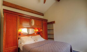 Ein Schlafzimmer mit einem Holzkopfteil, einem großen Spiegel, zwei Nachttischlampen und einem Bett mit grauer Decke.