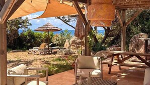 An outdoor seating area with wooden furniture, a table with bottles, and a view of the ocean. - Les Pieds dans l'eau (COTI CHIAVARI)