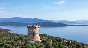 Ein historischer Turm, umgeben von üppigem Grün und einem stillen See, mit Bergen im Hintergrund.