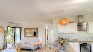 A modern kitchen with white cabinets, stainless steel appliances, and a dining area with a table set for two. - Les Pieds dans l'eau (COTI CHIAVARI)