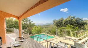 Ein Poolbereich mit Blick auf die Landschaft, eine überdachte Terrasse und Sitzmöglichkeiten im Freien.