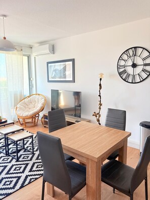 A modern living room with a dining table, chairs, a television, a framed picture, and a wall clock. - Beautiful setting with a terrace overlooking the sea (Saint-Cyprien)