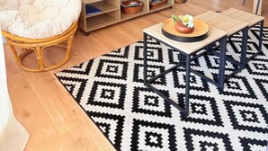 A living room with a television, a wicker chair, a coffee table, a patterned rug, and a kitchen area in the background. - Beautiful setting with a terrace overlooking the sea (Saint-Cyprien)