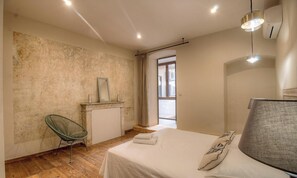 Ein Schlafzimmer mit einem Bett, einem Sessel, einem Schminktisch mit Spiegel und einem Fenster.